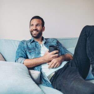 Man smiling on a couch while holding a mug